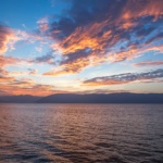 A vibrant sunset with dramatic clouds reflects over the calm ocean, capturing nature's beauty.