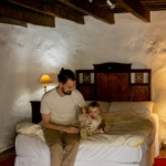 Father and child enjoy a bonding moment in a rustic bedroom setting, creating warmth and intimacy.