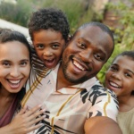 A joyful multicultural family taking a selfie outdoors in a lush garden setting.
