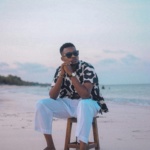 Man in stylish attire sits at the serene beach during sunset, enjoying the tranquil sea breeze.
