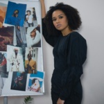 Stylish woman with afro hair in black dress standing by an inspiration board with fashion photos.