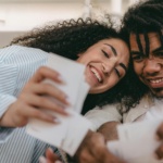 Smiling interracial couple enjoying memories together, looking at photos indoors. Warm and candid moment.