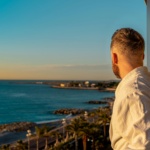 Man in bathrobe enjoys tranquil coastal view from balcony in Nice, France during sunrise.